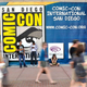 A photo of an SDCC banner outside the San Diego Convention Center with various fans walking and blurred in the foreground.